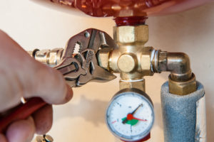 a close up of a hand and wrench working plumbing services on a pipe