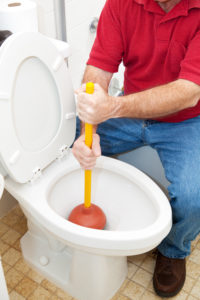 man conducting toilet repair with a plunger