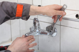 Plumber hands fixing water tap with spanner